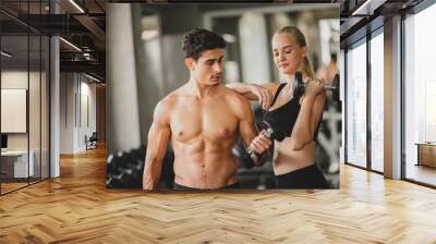 Handsome young shirtless man with beautiful woman in sportswear practicing weight lifting in modern gym for a fit and healthy body Wall mural