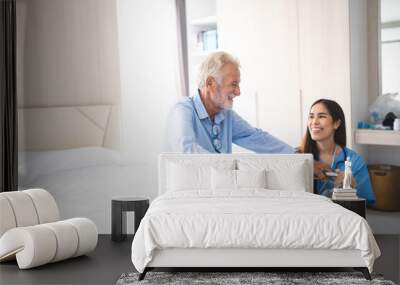 Portrait of Asian young nurse helping old elderly disable man grandfather to walk by using walker equipment in the bedroom. Senior patient of nursing home moving with walking frame and nurse support Wall mural