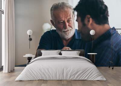 Sweet bonding. Cheerful elderly man sitting on the sofa next to his adult son, hugging him and posing together with him, concept of Father's Day Wall mural