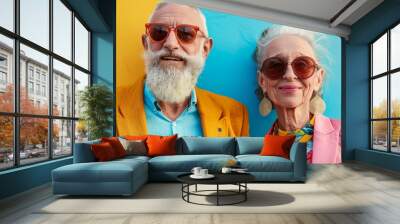 Fashionable senior couple wearing bright clothing and sunglasses, smiling against a vibrant yellow and blue background. Wall mural