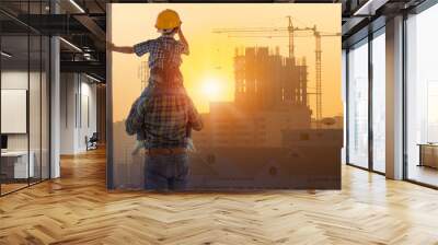 Asian boy on father's shoulders with background of new high buildings and silhouette construction cranes of evening sunset, father and son concept Wall mural