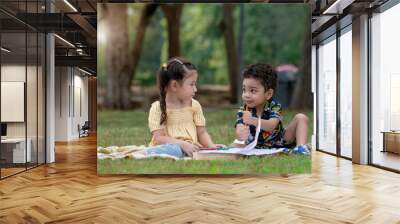 Boy and girl playing on lawn, cute little children sitting draw together in nature outdoor at park Wall mural