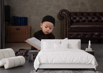 Cute little Muslim boy wearing traditional cloth sit on praying mat and interested in the Quran the Holy book of Muslims Wall mural