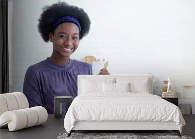 Healthy African woman holding a glass of milk after drinking in the kitchen, smiling with milk mustache on upper lip, smile with camera Wall mural