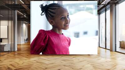 Portrait of cute African little girl with African braided hair wearing pink posing and smiling happily at someone Wall mural