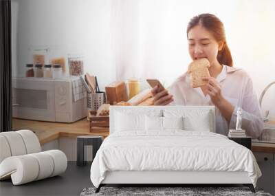 Young Asian woman in the kitchen prepare and eating sandwich for breakfast Wall mural