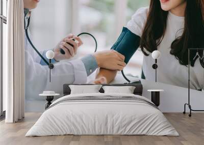 Doctor using sphygmomanometer with stethoscope checking blood pressure to a patient in the hospital. Wall mural