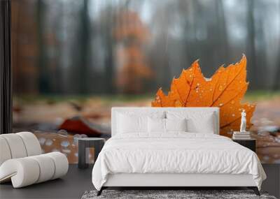 A vibrant orange leaf adorned with water droplets, resting on a bed of autumn leaves, evoking the beauty of nature. Wall mural