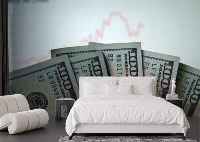 a bunch of 100 dollar bills in focus in the foreground of the picture. In the background a stock market graph, blurred. Taken inside in front a computer screen Wall mural