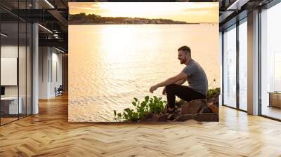 hombre joven apreciando el atardecer frente a un rio  Wall mural