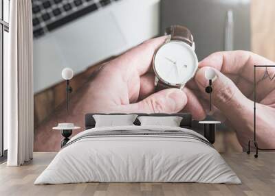 man setting his wristwatch against laptop computer and personal organizer on wooden desk Wall mural