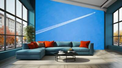 Jet with contrails flying across blue sky Wall mural