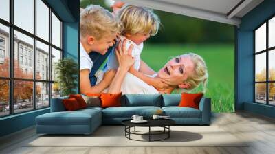 woman romps with her two sons on the grass Wall mural