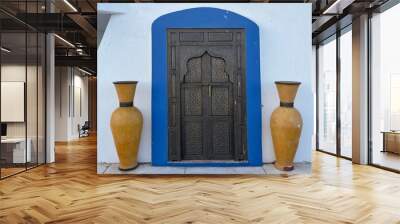 Old ornate iron or steel door with wooden frame and blue stone arch and two orange vases  Wall mural