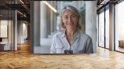 smiling middle aged woman in business casual attire, looking at the camera, background features modern office building, copy and text space, 16:9 Wall mural