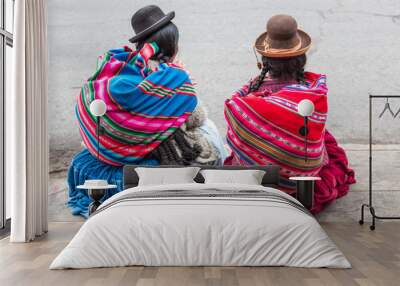 Two women with braids wearing traditional clothes sit on the streets of Puno city in Peru Wall mural