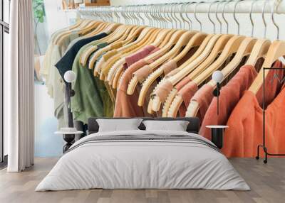 long rack with women's clothing arranged in rainbow order hanging from wooden hangers Wall mural