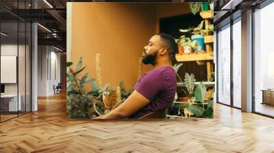 Relaxing portrait of a black gardener sitting in his nursery Wall mural