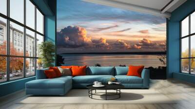 impressive billowing cumulus clouds at dusk along the horizon and reflecting in the sea. The clouds are highlighted by the gold, red glow of the sunset. Wall mural