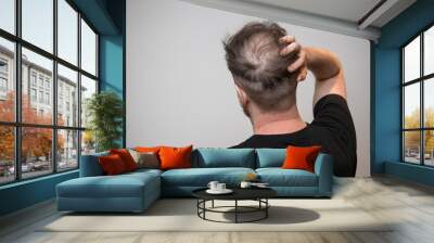 A single young caucasian male checking his bald patch on the back of his head, which shows clear signs of balding and hair loss. Shot against a white background with isolated man and room for text.  Wall mural