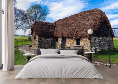 Leanach Cottage is shown preserved on the Colluden Battlefield near Inverness, Scotland. The stone foundation and thatched roof structure was likely built in the 1700s and used during battle in 1746. Wall mural