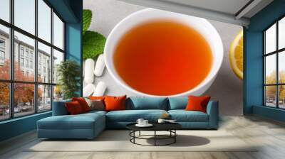 A cup of herbal tea surrounded by fresh lemon halves, mint leaves, and various health supplements, representing a natural wellness and immune-boosting setup Wall mural