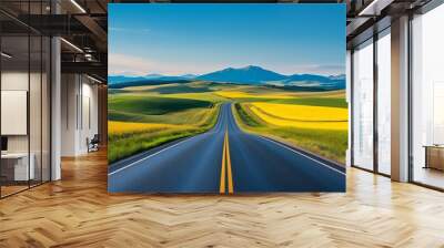 A broad view of a highway cutting through a picturesque landscape of diverse fields, including vibrant yellow canola, lush green crops, and golden harvested land with clear blue sky  Wall mural