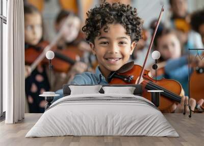 A joyful young boy with curly hair proudly plays the violin among a group of children practicing in an orchestra setting Wall mural