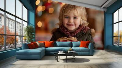 A blond boy in a winter coat holding a gift box happily on the day of the celebration, an important holiday event Wall mural