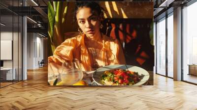 A woman sits at a table with a plate of food in a restaurant at lunch time. Wall mural