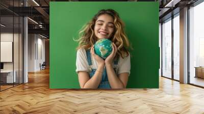 photograph of Joyful young woman holding Earth globe on green background for Earth Day Wall mural