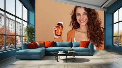 Smiling young woman holding a bottle of vitamins to nourish her body for good health. Wall mural