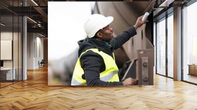 African American railroad engineer wearing safety equipment (helmet and jacket) checking gear train Wall mural