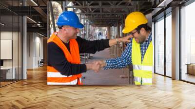 Construction worker and young architect shaking hands at construction site Wall mural