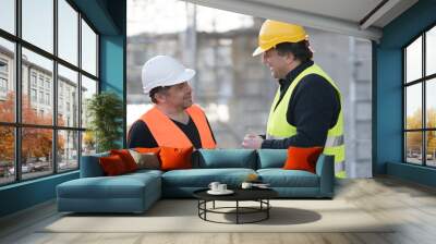 Two happy civil engineers wearing protective vests and helmets at work on construction site Wall mural