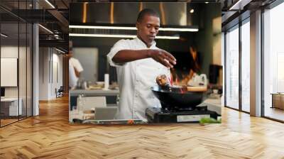 Black man, chef and seasoning with frying pan in kitchen at restaurant for fine dining, meal and creativity. Employee, professional and cook with food for culinary, hospitality and catering service Wall mural