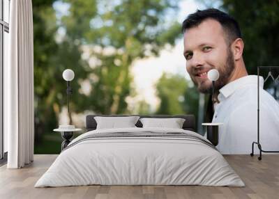 Portrait of caucasian man on urban park background. Cheerful male wearing white casual shirt. Smiling adult guy at the garden. Handsome young confident boyfriend Wall mural