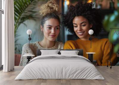 two women sitting in a relaxed setting on a couch, looking at something on a tablet, engaging in a friendly discussion and digital viewing Wall mural