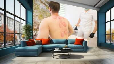 Young man sitting at the massage table and showing the hijama treatment scar. Wall mural