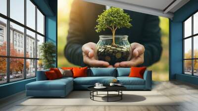 A jar of coins with a small tree growing from it, held by hands, illustrating the balance between wealth creation and environmental care. Wall mural