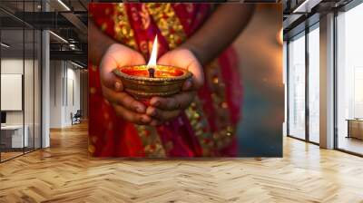 An Indian family dressed in traditional attire celebrating the Diwali festival by lighting an oil lamp at home, with a young girl holding the lamp. Wall mural