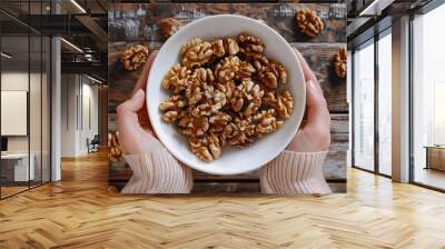 Bowl of walnuts in woman's hands, handful of unshelled nuts, cracked nut, woman holds nuts in white bowl, nourishing nutrients, healthy diet, wooden backdrop, top-down view, premium image. Wall mural