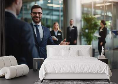 Businessman extending hand to welcome new team member in contemporary workplace with coworkers in the backdrop. Wall mural