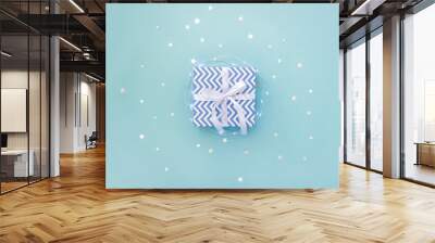 Present box with blue chevron pattern and white bow on pastel background surrounded by light garland and star confetti. Minimal concept of Christmas. Top view, flat lay Wall mural