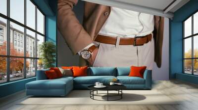 Closeup fashion image of luxury watch on wrist of man.body detail of a business man.Man's hand in brown pants pocket closeup at white background.Man wearing brown jacket and white shirt.Toned. Wall mural