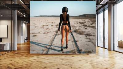 Full length image of Sexy fashion female biker girl in black helmet in dessert. Young beautiful model in black crop top and bikini suit walking away in desert USA. Back view, horizontal, copy space. Wall mural