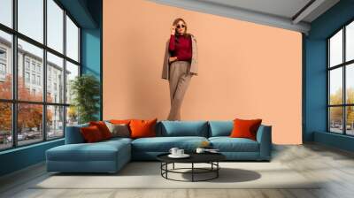 Full length studio portrait of young business woman. Full length portrait of smiling attractive businesswoman in suit posing while standing with arms crossed and looking at camera isolated over beige Wall mural