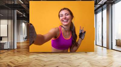 Image of a positive young brunette sports fitness woman posing isolated over white wall background take selfie by camera showing peace gesture.Attractive girl making a selfie after her exercise. Wall mural