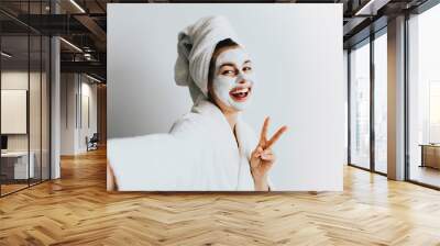 Self portrait of charming, stylish, pretty, model after bath wrapped in towel shooting selfie on front camera applying using face mask for her dry, oiled, sensual face skin, enjoying procedure Wall mural