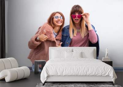 Two happy young female friends giving a thumbs up gesture of approval and success Close up fashion portrait of Two cheerful beautiful girls friends posing for camera outdoor, colourful jackets. Wall mural